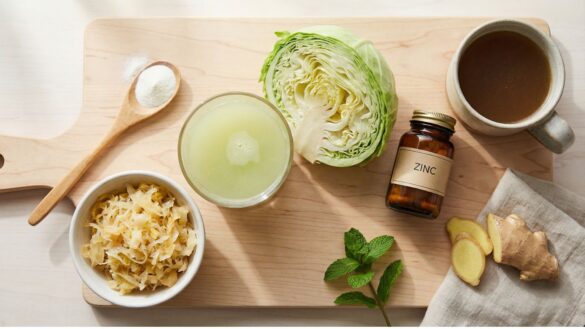 Natural gut inflammation remedies including fresh cabbage juice, sauerkraut, supplements and bone broth arranged on wooden cutting board