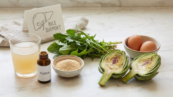Natural bile flow remedies including TUDCA supplement, apple cider vinegar, dandelion greens, artichoke and eggs arranged on marble surface